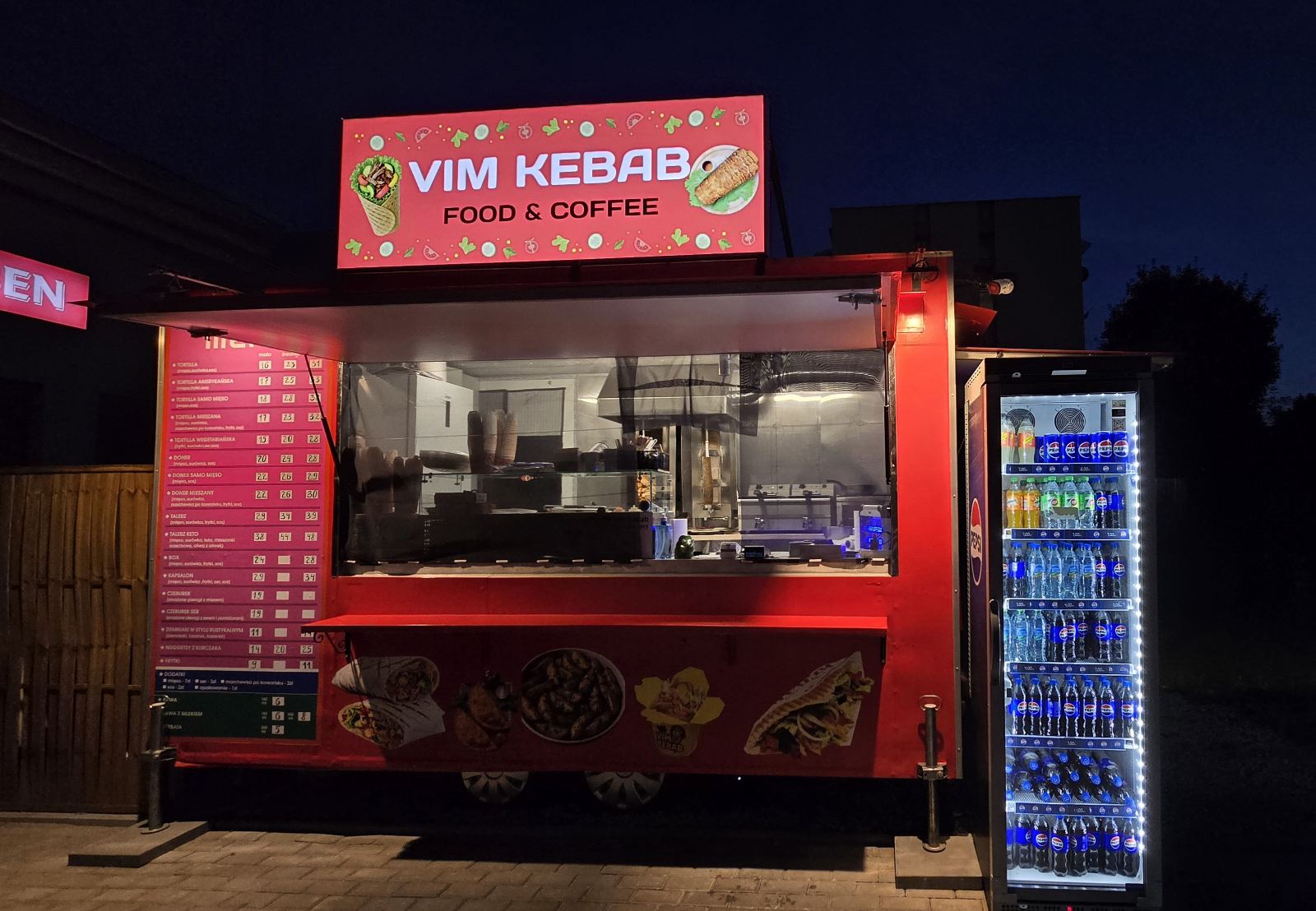 Czerwony food truck VIM Kebab nocą, podświetlone menu, otwarte okno serwisowe i lodówka Pepsi z niebieskim podświetleniem.